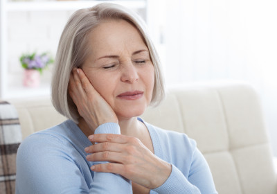 An older woman holds her hand to her ear in mild discomfort due to tinnitus